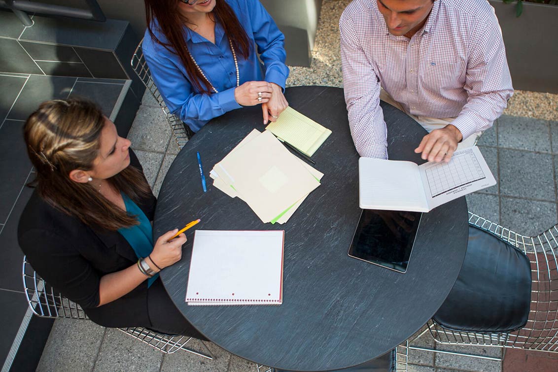 Photo of 3 people at a table having a meeting outside