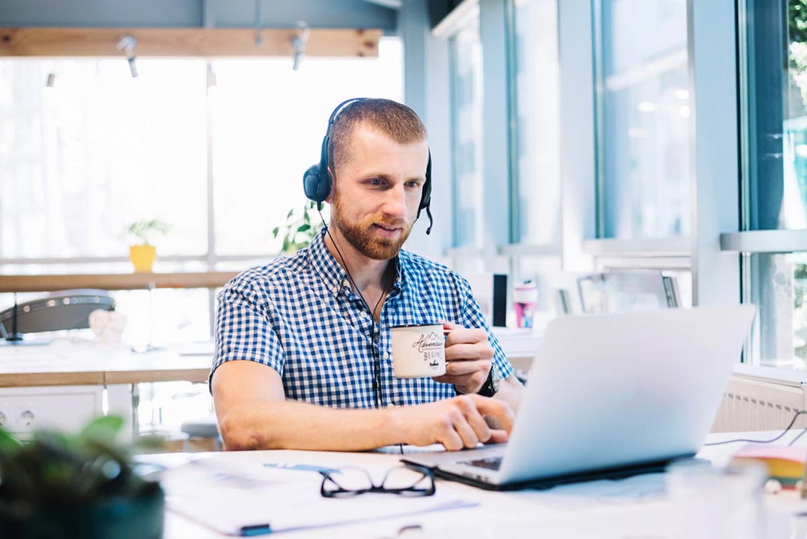 Photo of a man having coffee and using a laptop