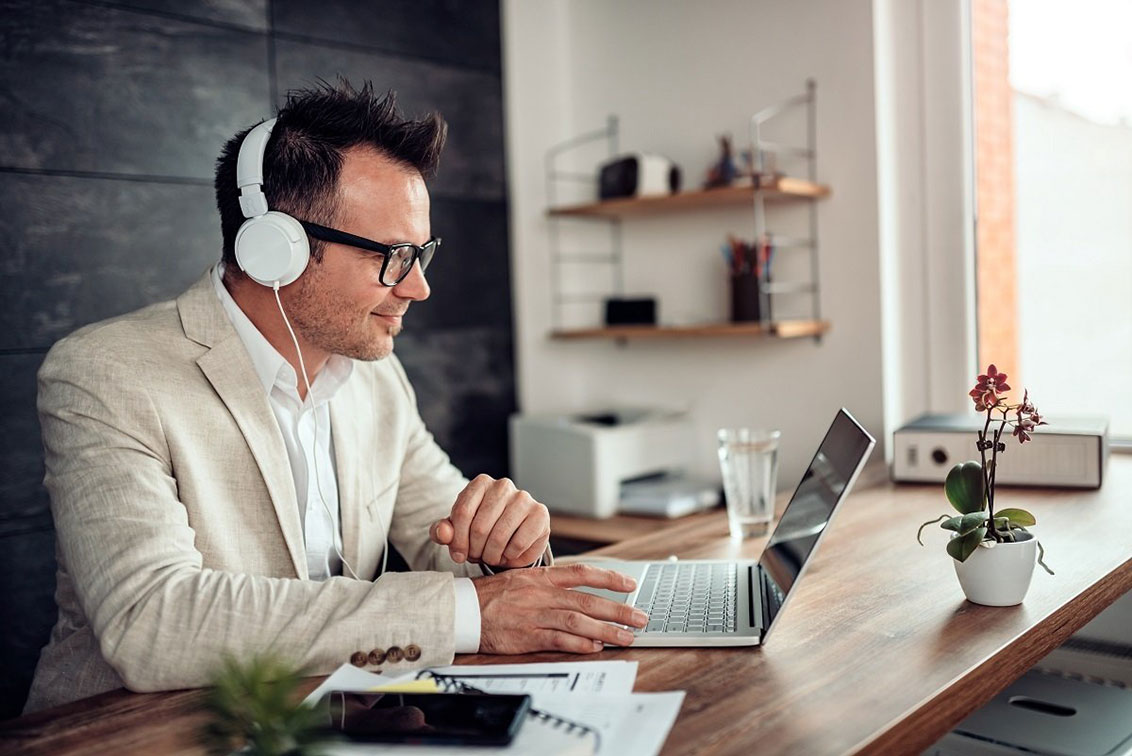 Photo of a man using a laptop and wearing headphones