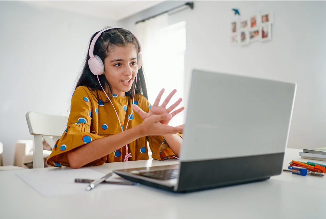 Photo of a little girl wearing headphones and using a laptop