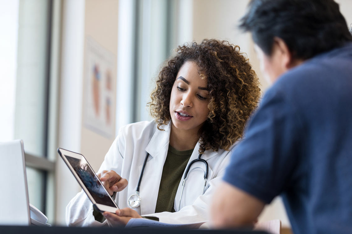 The mid adult female doctor uses the digital tablet to show the x-ray to the unrecognizable senior man