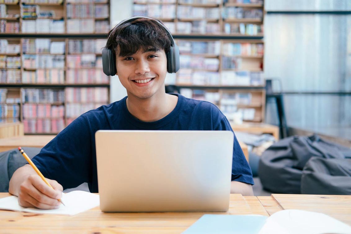 Photo of smiling male student in a library with a laptop