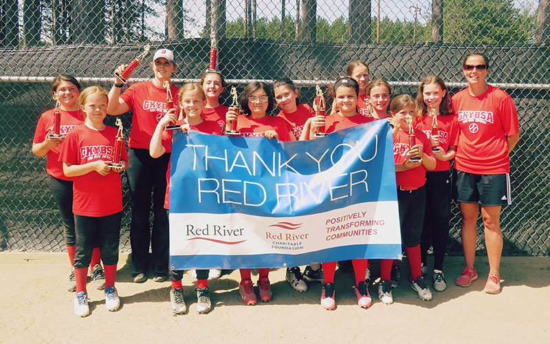 Photo of girls softball team with trophies and thank you sign